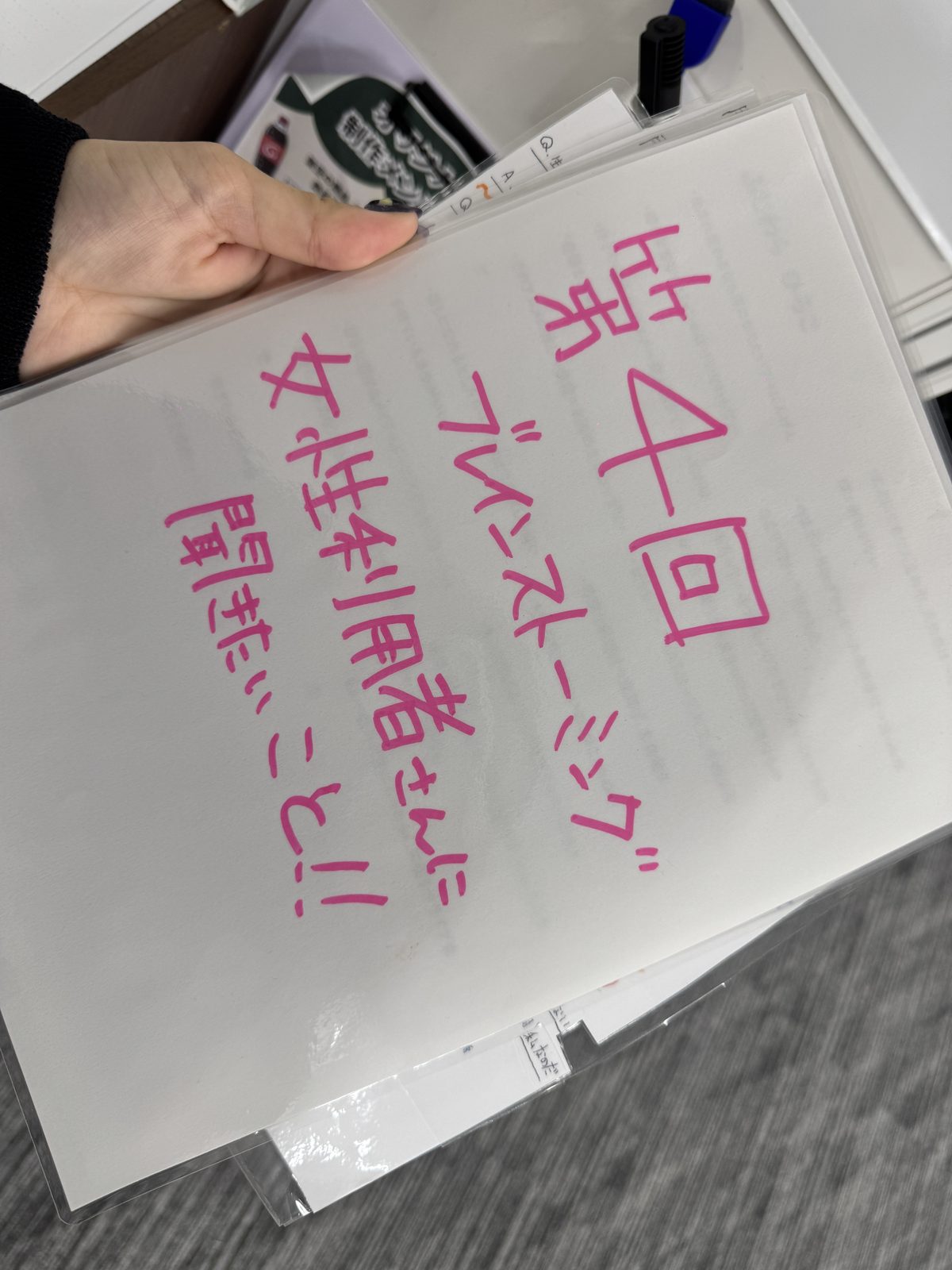 ピンクのマーカーで「第4回 ブレインストーミング 女性利用者さんに聞きたいこと!!」と書かれたお題シートを職員が手に持っている様子