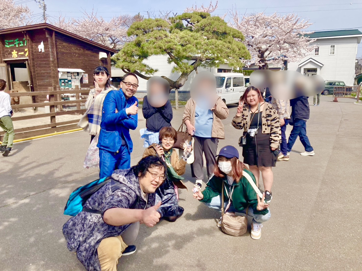 桜の名所で、利用者さんとスタッフが並んで笑顔の記念撮影をしている様子