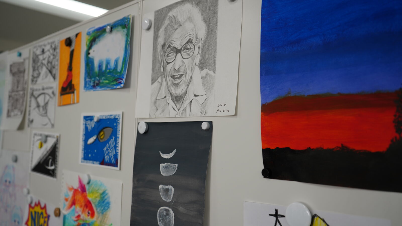 壁に並ぶ利用者さんの作品。鉛筆の人物画や、夕焼けを描いた絵、月の満ち欠けの絵など
