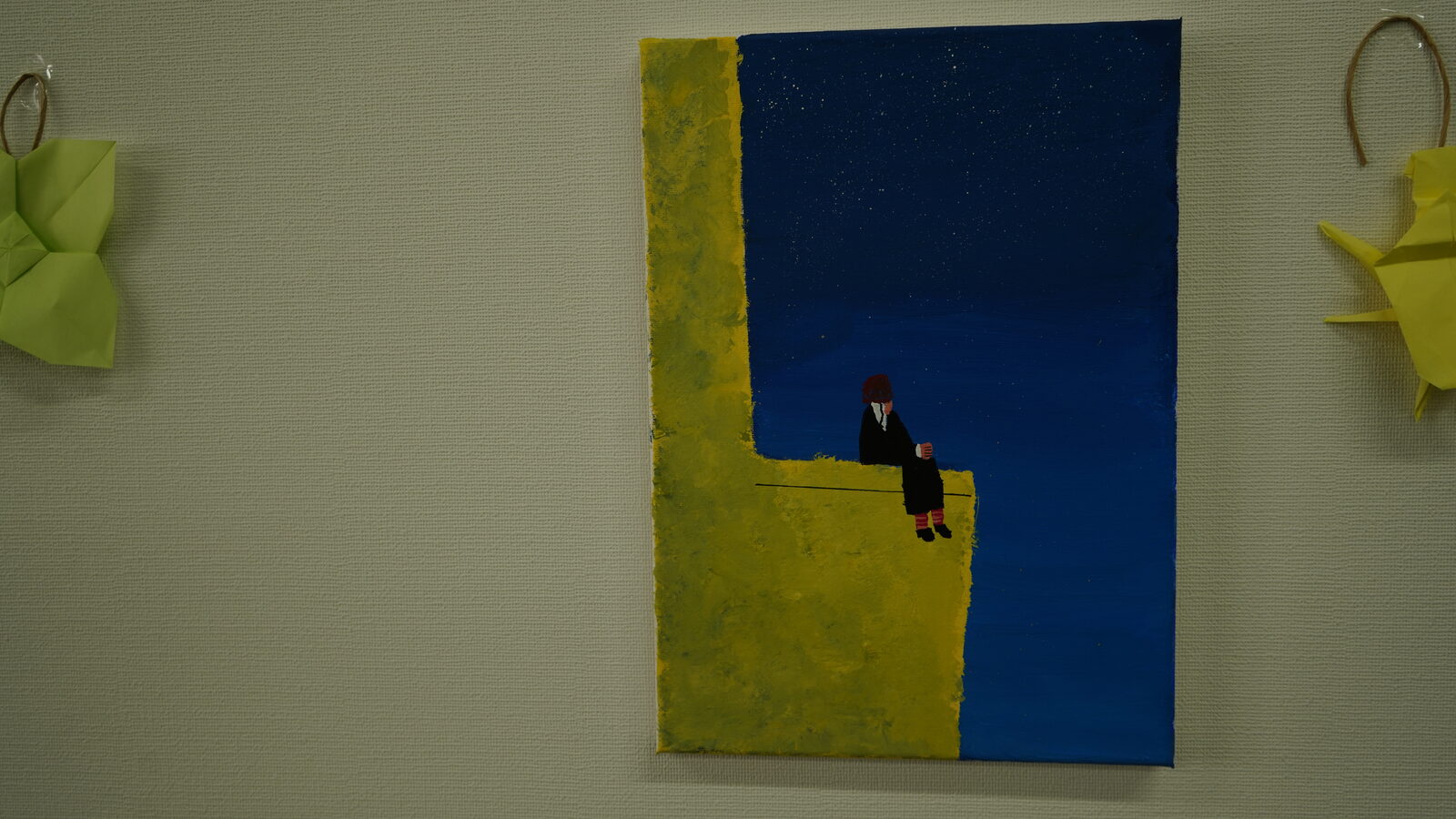壁に飾られた、青い夜空と黄色い壁の間に人が座っている絵