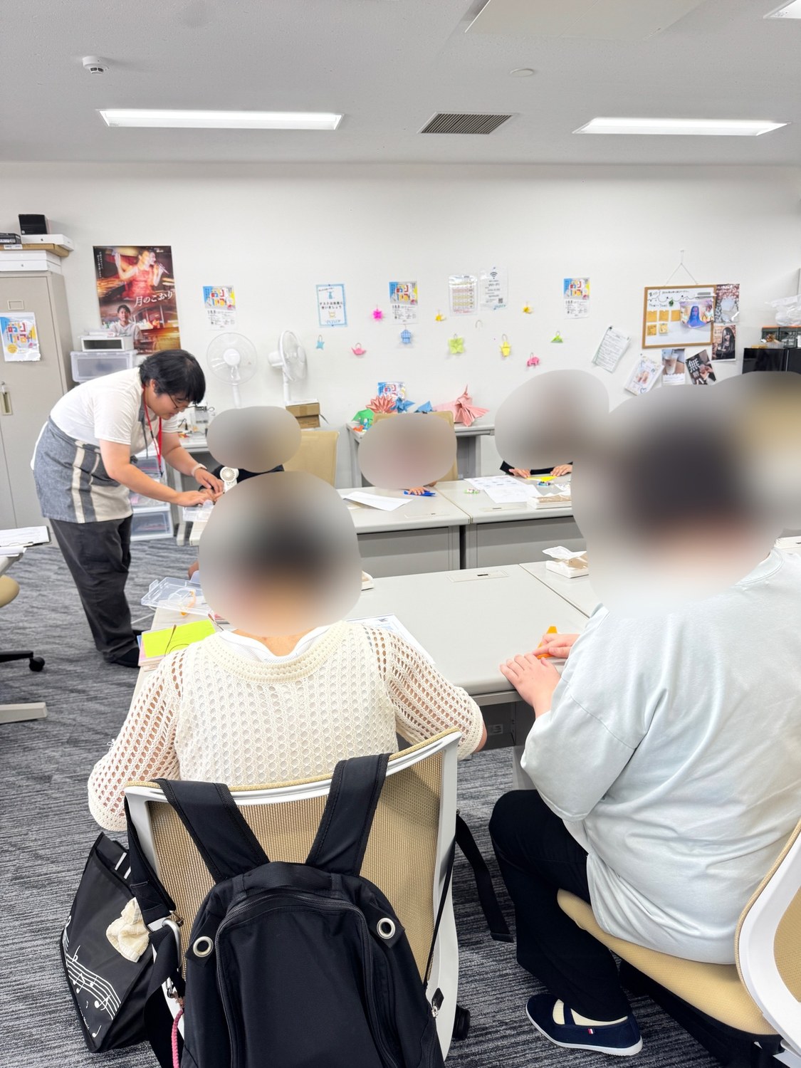 PONOの室内に机を並べたワークショップ会場。参加者が机を囲んで折り紙に取り組み、エプロン姿のスタッフが横についてサポートしている様子