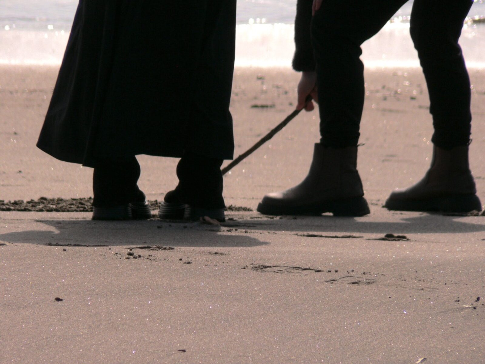 棒を手に砂浜に絵を描く利用者さんたちの足元